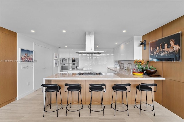 kitchen with kitchen peninsula, island exhaust hood, tasteful backsplash, a breakfast bar, and white cabinets