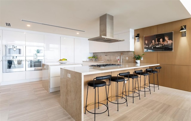 kitchen with island exhaust hood, kitchen peninsula, tasteful backsplash, white cabinets, and stainless steel gas stovetop