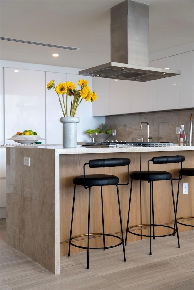 kitchen with a kitchen bar, island exhaust hood, white cabinetry, and tasteful backsplash