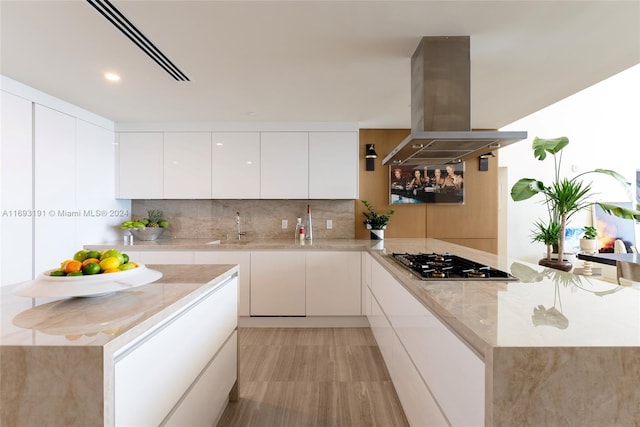 kitchen with white cabinetry, sink, stainless steel gas cooktop, tasteful backsplash, and island range hood