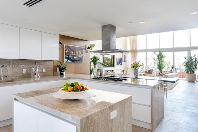 kitchen with decorative backsplash, stainless steel gas cooktop, white cabinetry, and range hood