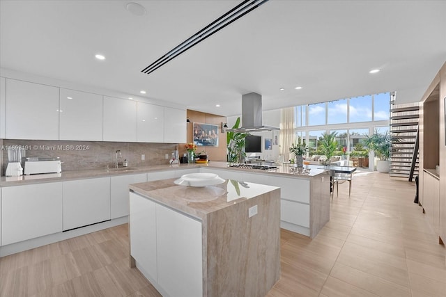 kitchen featuring tasteful backsplash, a kitchen island, sink, exhaust hood, and white cabinetry