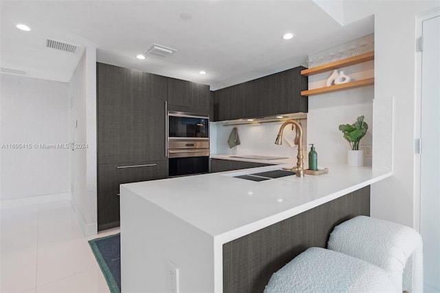 kitchen with a breakfast bar, stainless steel microwave, sink, light tile patterned flooring, and kitchen peninsula