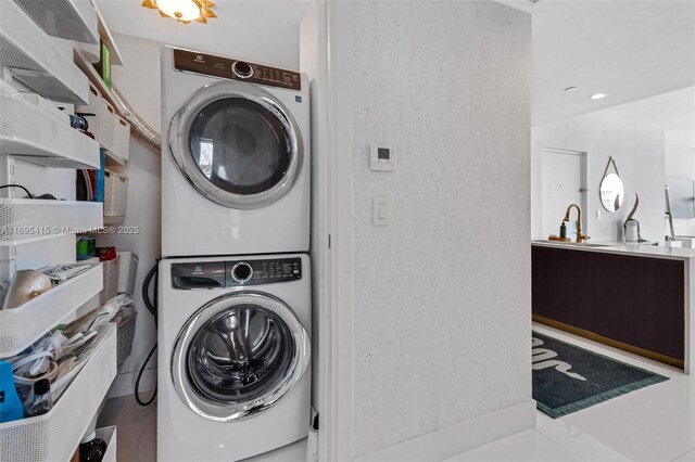 laundry room featuring tile patterned floors, stacked washing maching and dryer, and sink