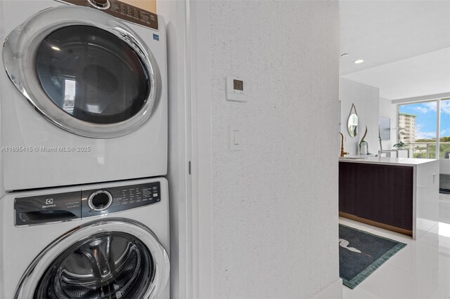 laundry room with light tile patterned floors, stacked washer and dryer, and sink