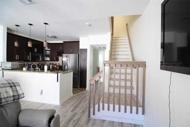 kitchen featuring pendant lighting, light hardwood / wood-style flooring, appliances with stainless steel finishes, light stone counters, and dark brown cabinetry