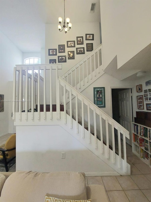 stairs with a towering ceiling, tile patterned floors, and a notable chandelier