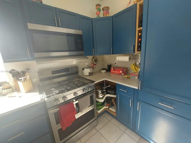 kitchen with light tile patterned floors, blue cabinetry, backsplash, and appliances with stainless steel finishes