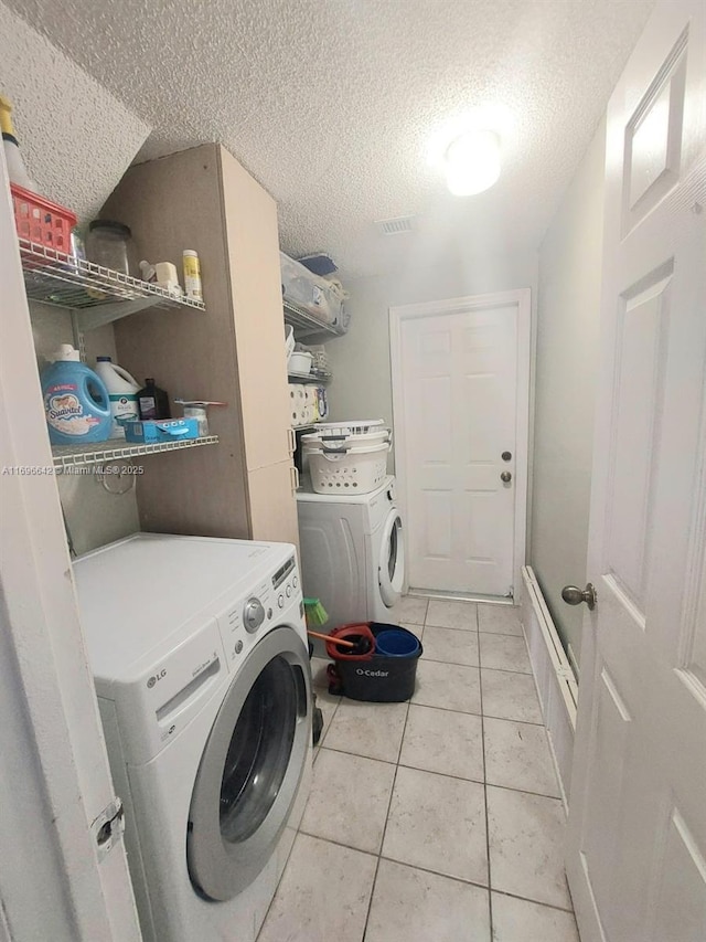 laundry room featuring a textured ceiling, light tile patterned floors, and washing machine and clothes dryer