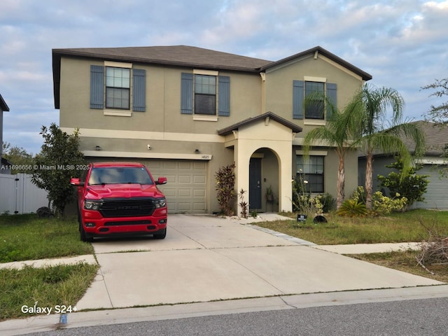 traditional-style home with concrete driveway, an attached garage, fence, and stucco siding