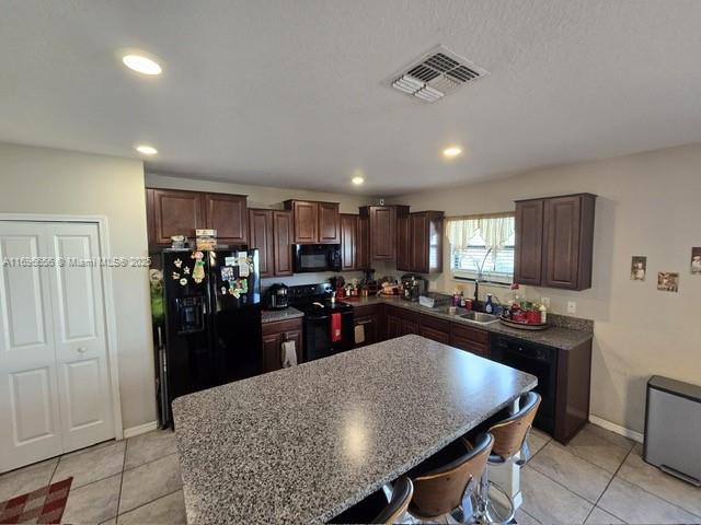 kitchen featuring a center island, visible vents, a sink, dark brown cabinets, and black appliances