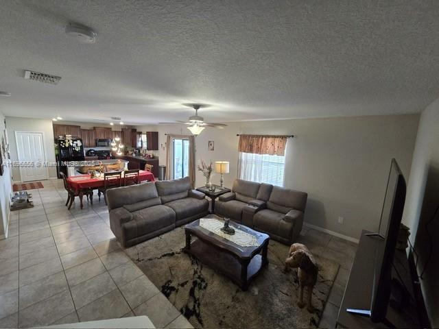 living room with visible vents, light tile patterned flooring, ceiling fan, a textured ceiling, and baseboards