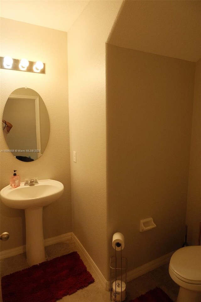 half bathroom with a sink, toilet, and baseboards