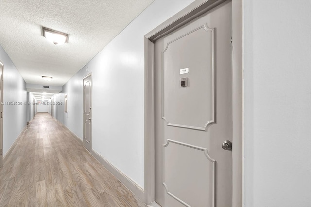 hallway with a textured ceiling, light wood finished floors, and baseboards