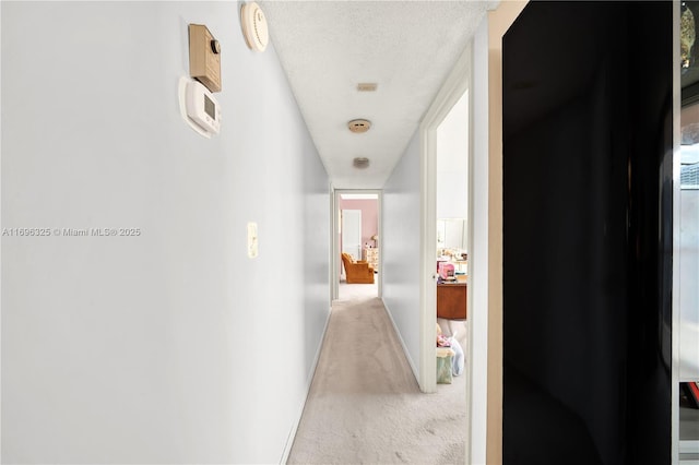 hall with a textured ceiling, baseboards, and light colored carpet