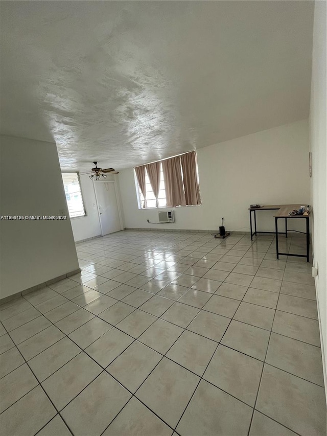 tiled empty room with ceiling fan, a wall mounted air conditioner, and a textured ceiling