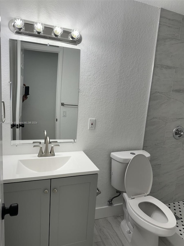 bathroom with tiled shower, vanity, and toilet