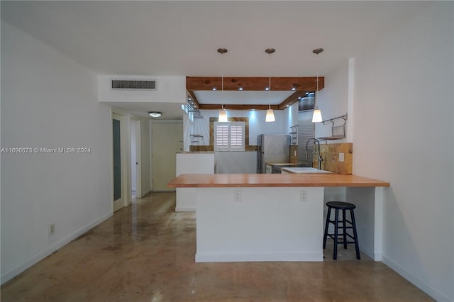 kitchen featuring pendant lighting, sink, a kitchen bar, kitchen peninsula, and stainless steel refrigerator