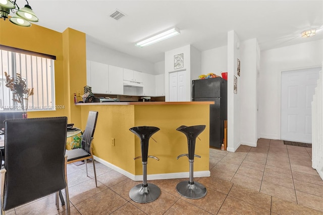 kitchen featuring white cabinets, kitchen peninsula, black fridge, and light tile patterned flooring