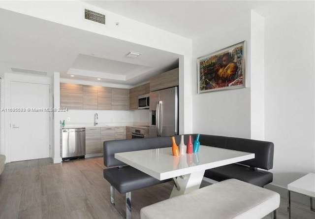 dining area featuring a raised ceiling, sink, and light hardwood / wood-style flooring