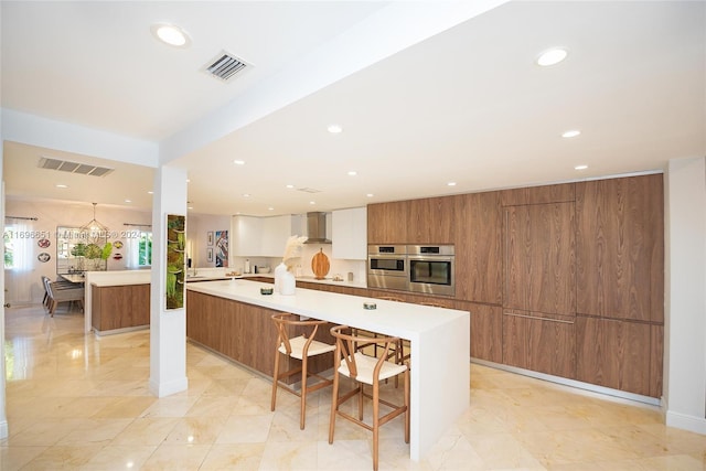 kitchen with a breakfast bar, a large island with sink, white cabinetry, and wall chimney exhaust hood