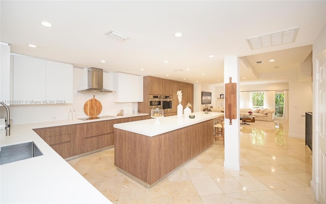 kitchen featuring a large island, sink, wall chimney exhaust hood, black electric cooktop, and white cabinets