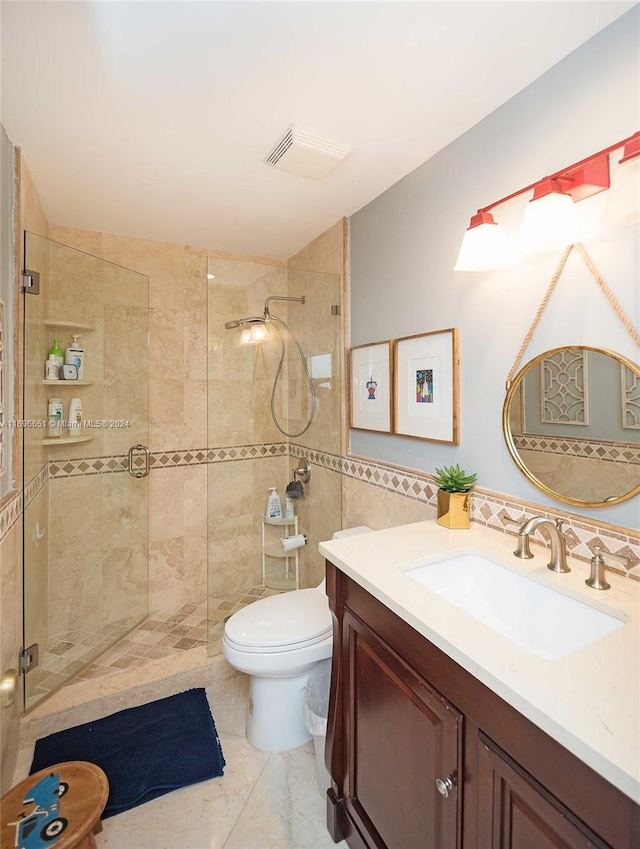 bathroom with vanity, tiled shower, tile walls, tile patterned flooring, and toilet