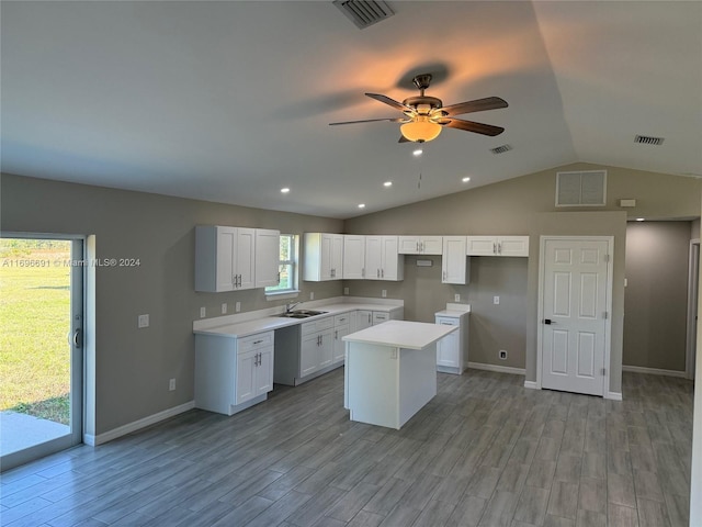 kitchen featuring white cabinets, a center island, light hardwood / wood-style flooring, and vaulted ceiling