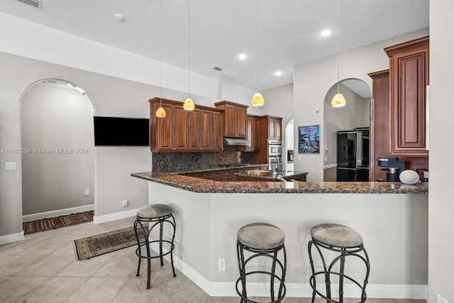 kitchen featuring tasteful backsplash, dark stone countertops, kitchen peninsula, decorative light fixtures, and black appliances