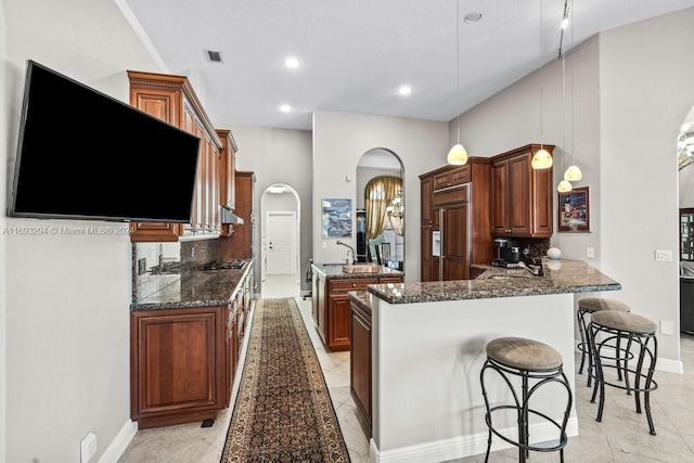 kitchen featuring dark stone counters, hanging light fixtures, decorative backsplash, paneled built in refrigerator, and kitchen peninsula