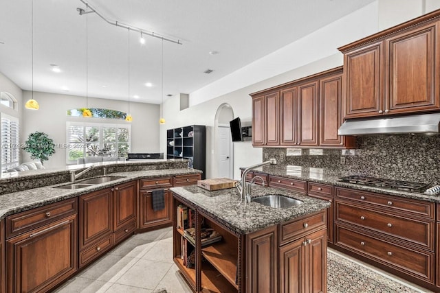 kitchen with pendant lighting, stainless steel gas stovetop, a kitchen island with sink, and sink