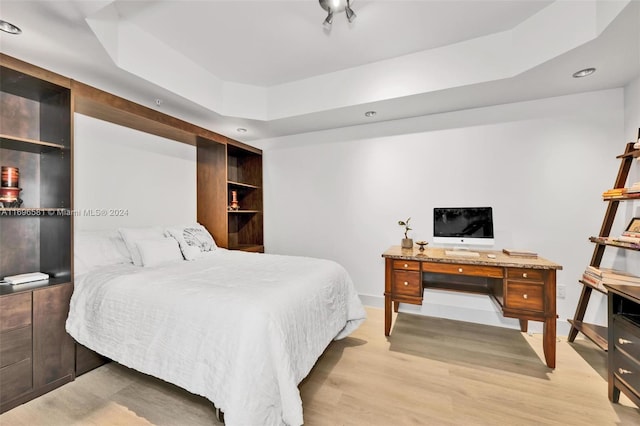 bedroom with light wood-type flooring and a tray ceiling