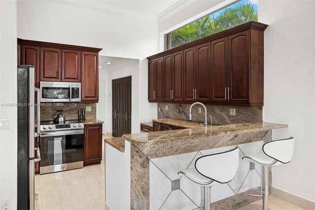 kitchen featuring tasteful backsplash, kitchen peninsula, light stone countertops, and appliances with stainless steel finishes