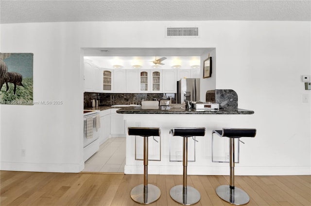 kitchen featuring white cabinetry, a kitchen breakfast bar, stainless steel refrigerator with ice dispenser, and white range with electric stovetop