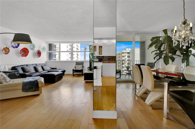 living room featuring a wealth of natural light, a notable chandelier, a textured ceiling, and light hardwood / wood-style flooring