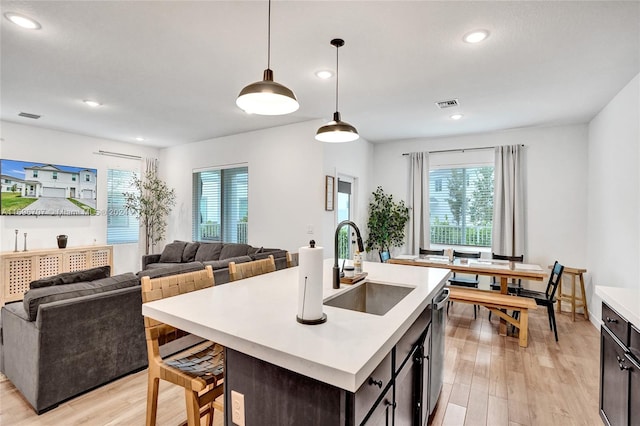 kitchen featuring a kitchen island with sink, sink, hanging light fixtures, stainless steel dishwasher, and light hardwood / wood-style floors