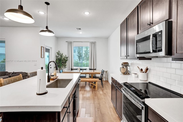 kitchen featuring a center island with sink, sink, light wood-type flooring, decorative light fixtures, and stainless steel appliances