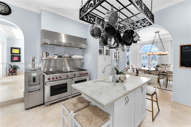 kitchen featuring double oven range, a kitchen island with sink, sink, wall chimney exhaust hood, and decorative light fixtures