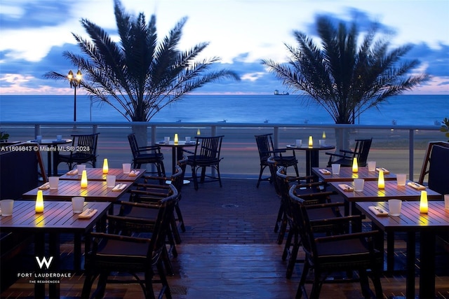 deck at dusk with a water view and a view of the beach