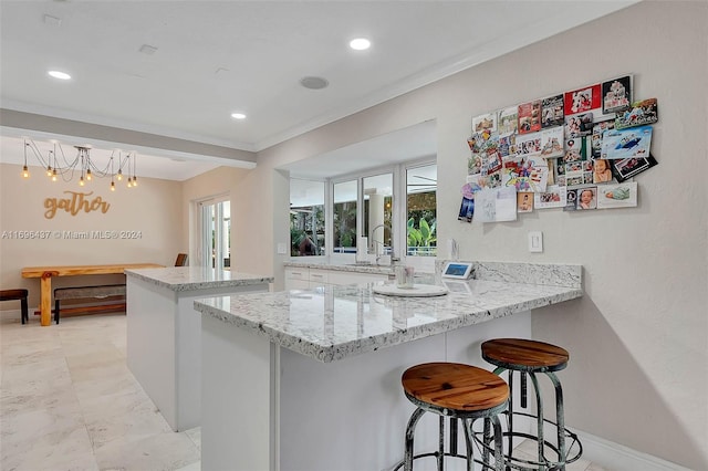 kitchen featuring a notable chandelier, kitchen peninsula, pendant lighting, a breakfast bar area, and ornamental molding