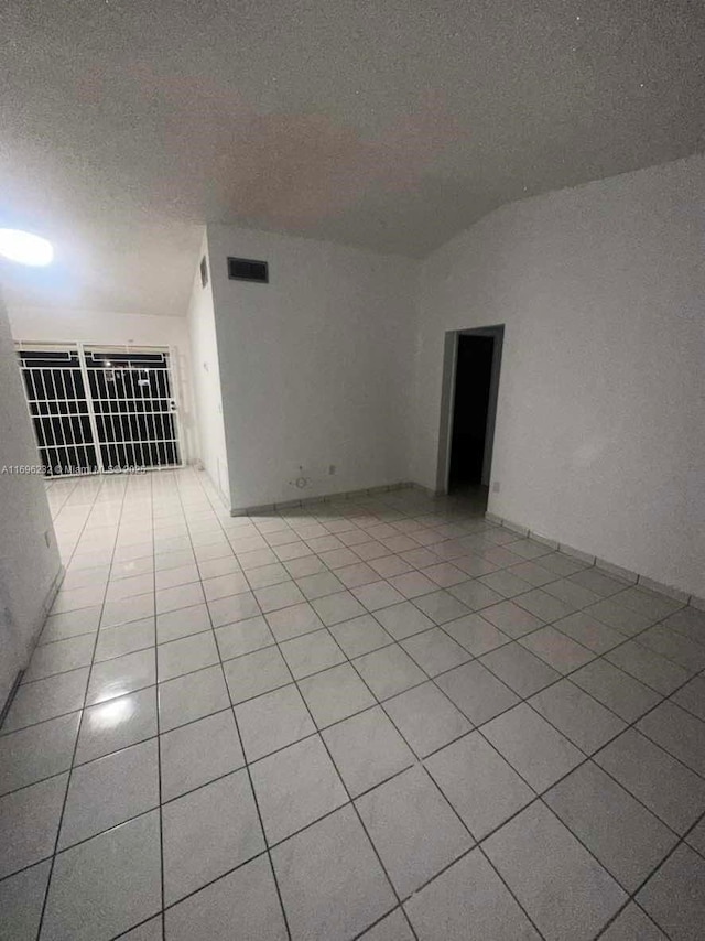 empty room with light tile patterned floors, a textured ceiling, and vaulted ceiling