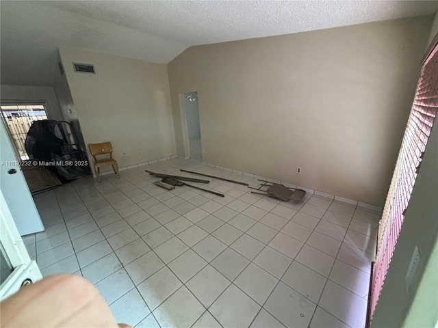 unfurnished living room with a textured ceiling, vaulted ceiling, and light tile patterned flooring