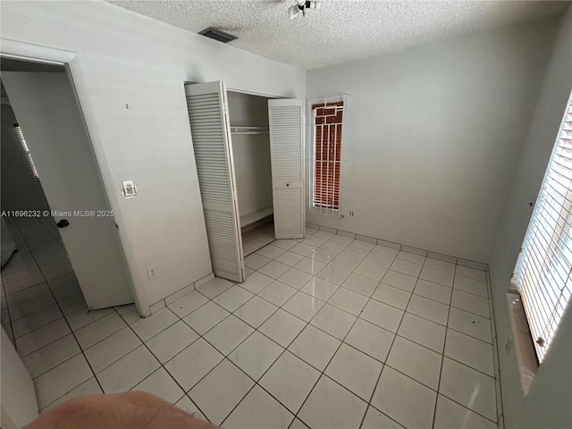 unfurnished bedroom featuring a closet, light tile patterned flooring, and a textured ceiling