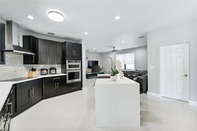 kitchen featuring a center island, wall chimney range hood, ceiling fan, black electric cooktop, and double oven