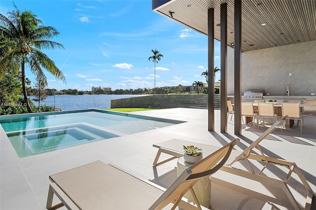 view of swimming pool with a patio area, a water view, exterior kitchen, and an in ground hot tub