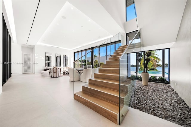 stairs with a water view, a raised ceiling, and plenty of natural light