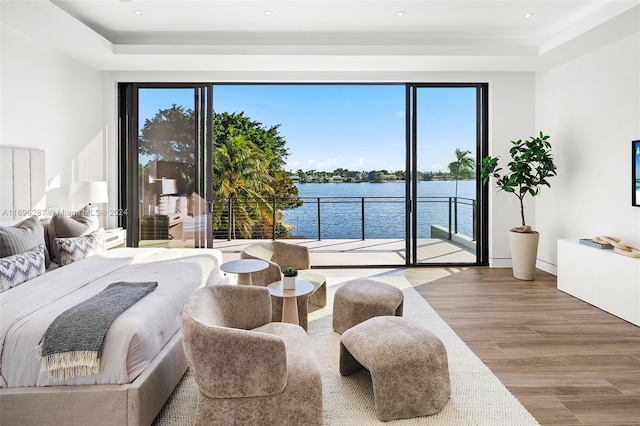 bedroom with a raised ceiling, a water view, wood-type flooring, and access to outside