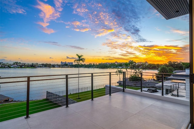 balcony at dusk featuring a water view