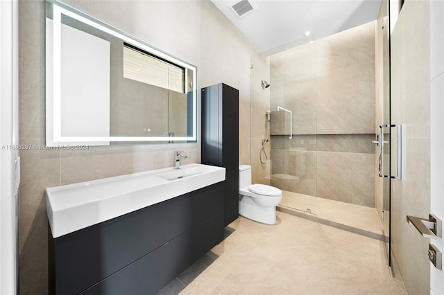 bathroom with a tile shower, vanity, toilet, and tile walls