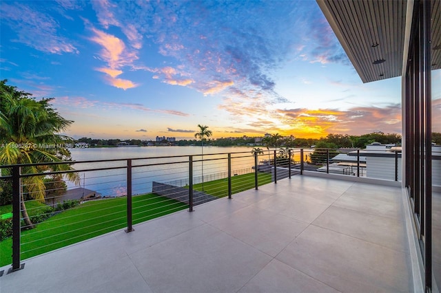 patio terrace at dusk with a yard, a water view, and a balcony